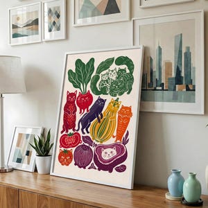 May include: A framed art print featuring a whimsical illustration of various cats integrated with vegetables and fruits. The composition includes red, orange, yellow, purple, and green produce shapes combined with feline figures in a flat, graphic style.