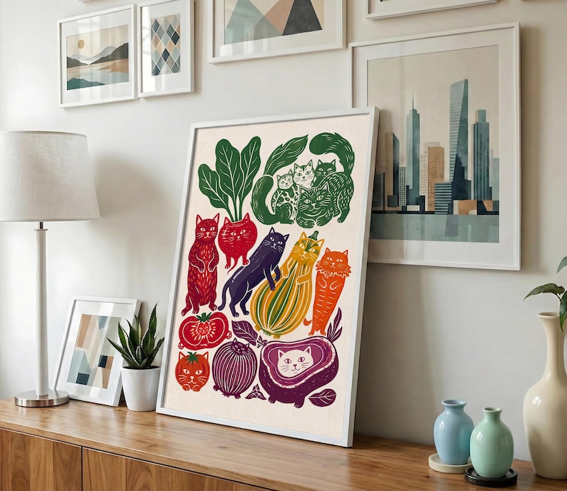 May include: A framed art print featuring a whimsical illustration of various cats integrated with vegetables and fruits. The composition includes red, orange, yellow, purple, and green produce shapes combined with feline figures in a flat, graphic style.