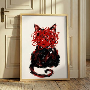 May include: Abstract art print of a black cat with a red scribble design over its face. The artwork is framed in a light wood frame and leans against a white door and wooden floor.
