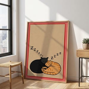 May include: A framed print featuring two sleeping cats, one black and one orange tabby, curled up together. The word "Zzzzzz" is above the cats. The print has a red border and a tan background.