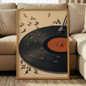 May include: A framed art print depicting a black vinyl record with a brown centre. Small cat illustrations are scattered across the record and the beige background. The print is in a light brown wooden frame.