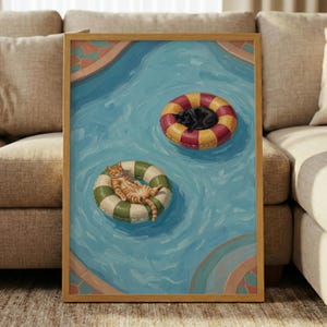 May include: A framed painting depicting a swimming pool with blue water and tiled edges. Two cats float on circular pool rings: an orange tabby cat rests on a green and white striped ring, while a black cat lies on a red and yellow striped ring.