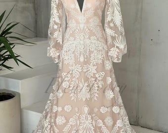 May include: A long-sleeved, white lace wedding dress with a V-neckline and a flowing skirt. The dress has a delicate floral pattern and a fringe detail at the hem.