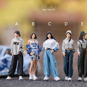 Può includere: Statuine di cinque figure alla moda in vari outfit casual, tra cui una felpa con la scritta "WX", un vestito fantasia con giacca e tute blu. Le figure sono in piedi di fronte a uno sfondo sfocato con un'auto blu. Il testo in alto recita "Cute Face Girl".