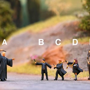 Könnte beinhalten: Eine Gruppe von fünf Miniaturfiguren, darunter ein Zauberer mit einem langen schwarzen Umhang und einem Zauberstab, und vier Schüler mit Zauberstäben und Hogwarts-Hausschals. Die Figuren stehen auf einem Weg vor einem felsigen Hügel.
