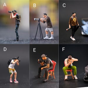 May include: Six miniature figurines of photographers, each with a different pose and holding a camera. The photographers are wearing casual clothing and are posed in various settings, including standing, sitting, and using a tripod.