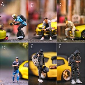 May include: Miniature figurines of people in various poses. One figure rides a unicycle, others sit or stand near yellow toy cars. The figures wear casual clothing, including jeans, hoodies, and sneakers. Some figures carry bags.
