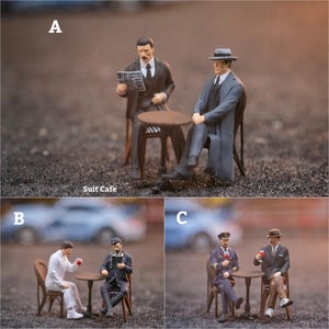 May include: Miniature figurines of men in suits and hats, seated at small tables, reading newspapers and drinking wine. The scene is labeled "Suit Cafe". The figures are in various poses, suggesting a cafe setting.