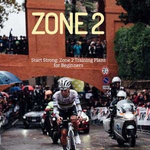Puede incluir: Un ciclista con un maillot blanco y negro con la palabra "UAE" en la parte delantera monta una bicicleta negra con un sillín amarillo y negro. El ciclista está pasando por un túnel con un arco de ladrillo rojo y las palabras "ZONE 2" en letras amarillas sobre el arco. El texto "Start Strong: Zone 2 Training Plans for Beginners" está debajo del arco. El texto "A.A by Theexcoach" está en la parte inferior de la imagen.