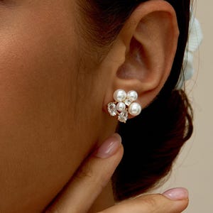 May include: Close-up of a cluster earring featuring faux pearls and clear crystals. The earring is a floral design with a mix of round pearls and sparkling crystals. The jewelry is set against a neutral background.
