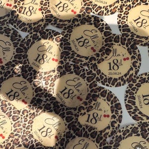 Può includere: Un set di adesivi rotondi, con stampa leopardata marrone e nera, con il testo "Ella's 18th" e la data "25.08.24" stampati in bianco.