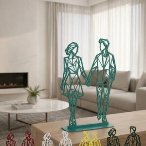 May include: Geometric metal sculptures of a couple holding hands, in various colors including green, red, white, and yellow. The figures have a modern, angular design and stand on rectangular bases. Home decor.