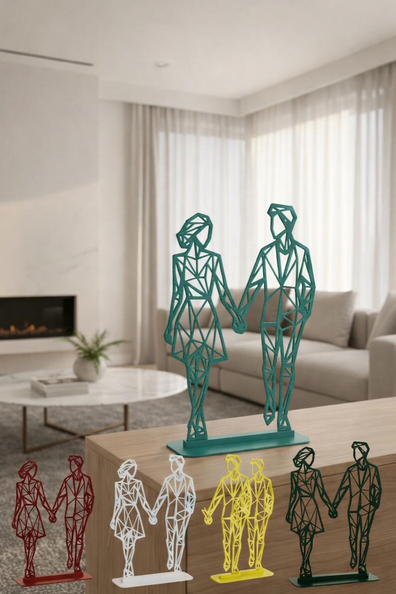 May include: Geometric metal sculptures of a couple holding hands, in various colors including green, red, white, and yellow. The figures have a modern, angular design and stand on rectangular bases. Home decor.