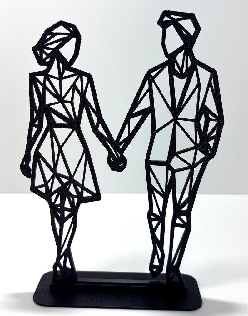 May include: Black metal sculpture of a couple holding hands. The figures are stylized with geometric shapes, standing on a rectangular base. The sculpture is a modern, minimalist design.