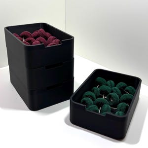 May include: Black rectangular containers filled with polishing wheels. One stack of three containers holds burgundy wheels, while a separate container holds green wheels. The containers are on a white surface.