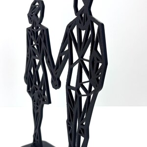 May include: A black geometric sculpture of a couple holding hands. The figures are stylized with a network of triangular shapes, mounted on a rectangular base. The sculpture is a modern, minimalist design.