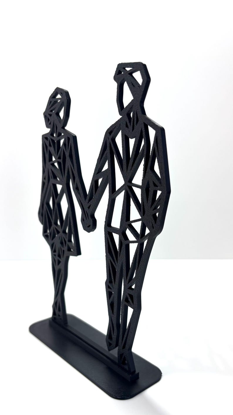 May include: A black geometric sculpture of a couple holding hands. The figures are stylized with a network of triangular shapes, mounted on a rectangular base. The sculpture is a modern, minimalist design.