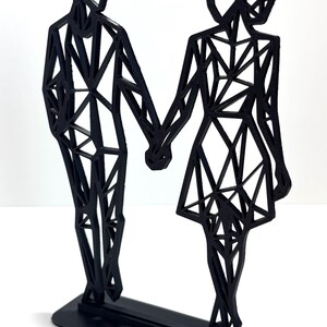 May include: Black geometric sculpture of a couple holding hands. The figures are stylized with angular shapes and stand on a rectangular base. A modern, minimalist design.