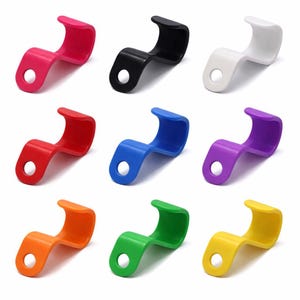 May include: Nine brightly coloured, curved plastic hooks. The hooks are in shades of pink, black, white, red, blue, purple, orange, green, and yellow. Each hook has a small hole at one end for hanging.