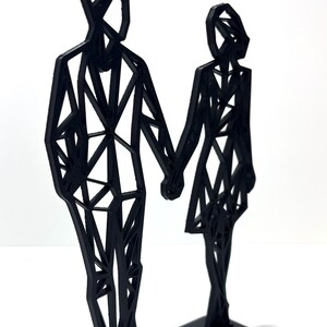 May include: A black geometric sculpture of a couple holding hands. The figures are stylized with angular shapes and stand on a rectangular base. The sculpture is made of a solid black material and is set against a white background.