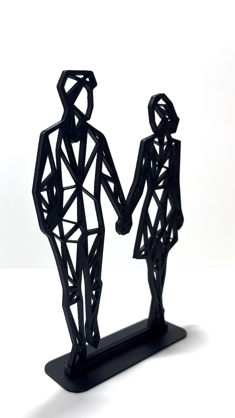 May include: A black geometric sculpture of a couple holding hands. The figures are stylized with angular shapes and stand on a rectangular base. The sculpture is made of a solid black material and is set against a white background.