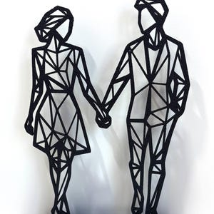May include: Black metal sculpture of a couple holding hands. The figures are stylized with geometric shapes, standing on a rectangular base. The sculpture is a modern, minimalist design.