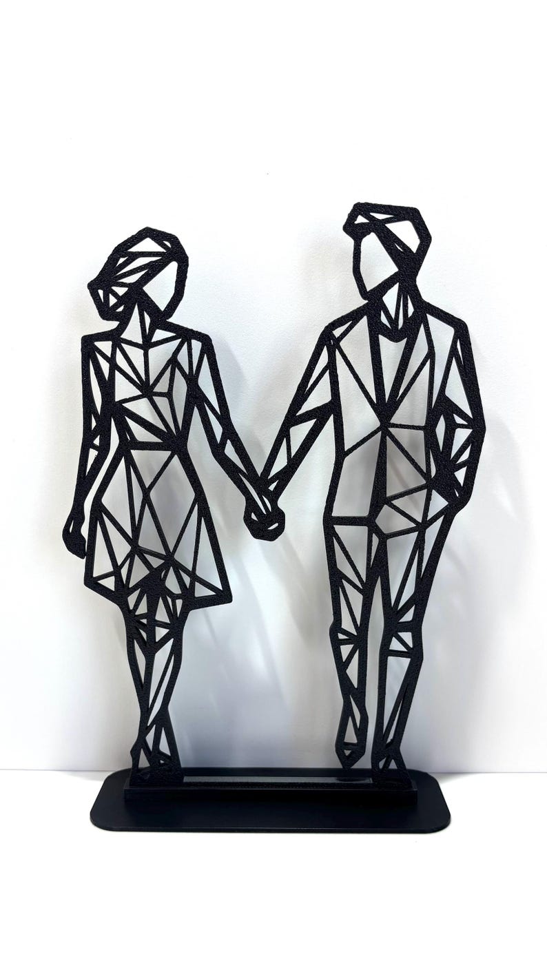 May include: Black metal sculpture of a couple holding hands. The figures are stylized with geometric shapes, standing on a rectangular base. The sculpture is a modern, minimalist design.