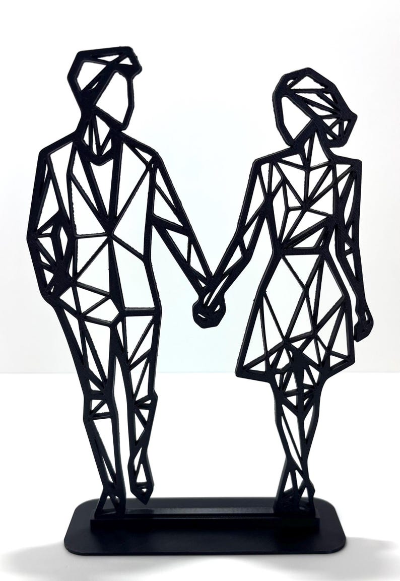 May include: A black geometric sculpture of a couple holding hands. The figures are stylized with angular shapes, standing on a rectangular base. The sculpture is made of a solid black material and set against a white background.