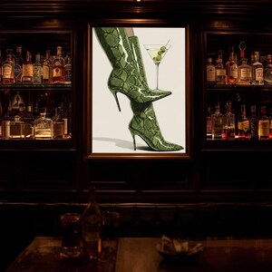 Op de afbeelding: Ingelijste kunst met groene, slangenleer-patroon hoge hakken en een martini glas met olijven. De afbeelding bevindt zich in een bar, met planken vol flessen op de achtergrond.