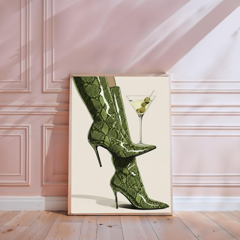 Op de afbeelding: Een ingelijste print met groene laarzen met slangenprint en een martini glas met olijven. Het kunstwerk staat tegen een neutrale achtergrond. De laarzen zijn in een dynamische pose geplaatst.