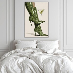 Op de afbeelding: Een artistieke print met een paar groene, slangenleer-achtige hoge hakken en een martini glas met olijven. De laarzen hebben stilettohakken en spitse tenen. Het martini glas voegt een vleugje elegantie toe.