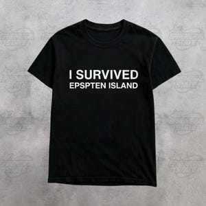 Puede incluir: Camiseta negra con el texto blanco "I SURVIVED EPSPTEN ISLAND". La camiseta tiene mangas cortas y cuello redondo. La prenda se muestra sobre un fondo gris.
