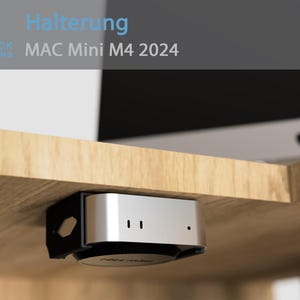 May include: A silver Mac Mini M4 2024 computer is mounted under a wooden desk using a black 3D printed bracket. The text "Halterung MAC Mini M4 2024" is visible in the top left corner of the image.