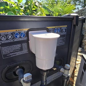 Può includere: Uno skimmer bianco per piscina attaccato a una struttura per piscina grigio scuro. Lo skimmer ha un corpo cilindrico e un coperchio. Le etichette di avvertimento sull'immersione e l'annegamento sono visibili.