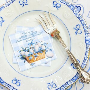 May include: A blue and white checkered card with a floral design and the text "But be of GOOD CHEER; I have overcome the world!" John 16:33. The card is on a white plate with a blue and white border.