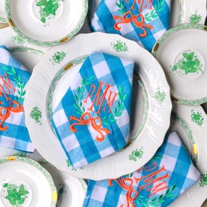 May include: Blue and white gingham napkins with embroidered green wreaths and orange bows. The napkins are monogrammed with the initials "PMM".