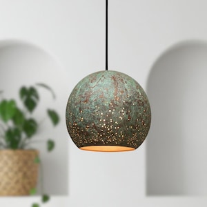 May include: A spherical pendant light fixture with a textured, verdigris finish. The lamp has numerous small perforations that emit a warm glow. The fixture hangs from a black cord. The overall design is modern and artistic.