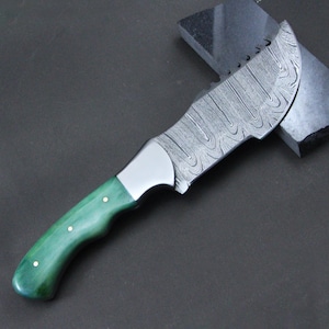 May include: A Damascus steel knife with a curved blade and a green wooden handle. The handle is accented with three small brass rivets. The blade has a unique, wavy pattern. The knife is designed for outdoor use.