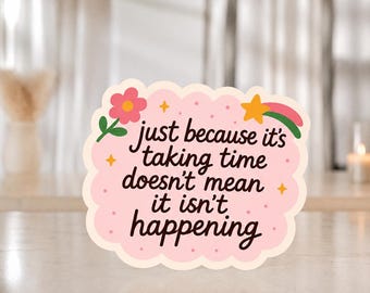 Puede incluir: Una pegatina de borde festoneado con fondo rosa claro con pequeños puntos, una flor rosa, una estrella amarilla y el texto: just because it's taking time doesn't mean it isn't happening. El diseño incluye un tallo verde y un trazo rosa.