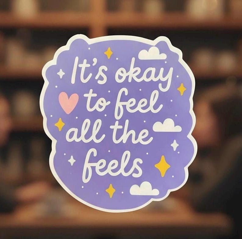 May include: A sticker with a light purple background and a white border. The sticker has the text "It's okay to feel all the feels" in white script. There is a pink heart, yellow stars, white clouds, and small white stars.