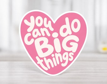 Könnte beinhalten: Ein pinkfarbener herzförmiger Aufkleber mit den Worten "you can do BIG things" in weißer, fetter Schrift. Der Aufkleber hat einen weißen Rand und liegt auf einer hellen Holzoberfläche.