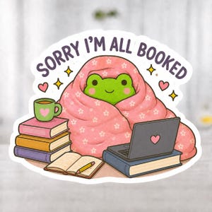 Könnte beinhalten: Ein Aufkleber mit einem grünen Frosch, der in eine rosa Decke mit Blumenmuster gehüllt ist. Der Frosch ist von Büchern, einem Laptop und einer Kaffeetasse umgeben. Der Text "SORRY I'M ALL BOOKED" steht darüber.