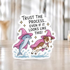 Può includere: Un adesivo fustellato raffigurante un delfino grigio e una mucca marrone e bianca, entrambi con cappelli da mago e mantelli glitterati rosa. Il testo recita "TRUST THE PROCESS... EVEN IF IT LOOKS LIKE THIS!" circondato da piccole stelle gialle e spruzzi d'acqua blu.