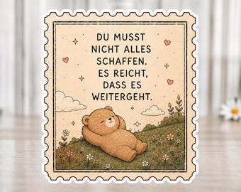 Könnte beinhalten: Ein Aufkleber mit einem Briefmarken-Design, das einen Cartoon-Bären zeigt, der sich auf einem grasbewachsenen Hügel mit Blumen entspannt. Der Text lautet: "Du musst nicht alles schaffen. Es reicht, dass es weitergeht."
