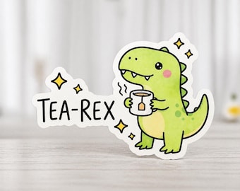 Könnte beinhalten: Ein Aufkleber mit einem grünen Dinosaurier, der eine Teetasse hält. Der Text "TEA-REX" ist in Schwarz geschrieben, mit gelben Sternakzenten. Der Dinosaurier hat rosa Wangen.