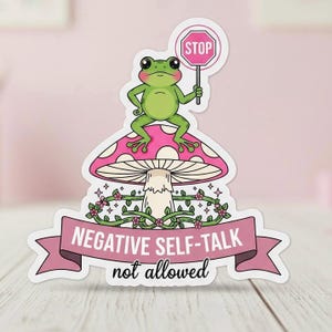 May include: A sticker showing a green frog with a "STOP" sign on a pink mushroom with white spots. A banner below reads "NEGATIVE SELF-TALK not allowed" in white text, with floral accents.