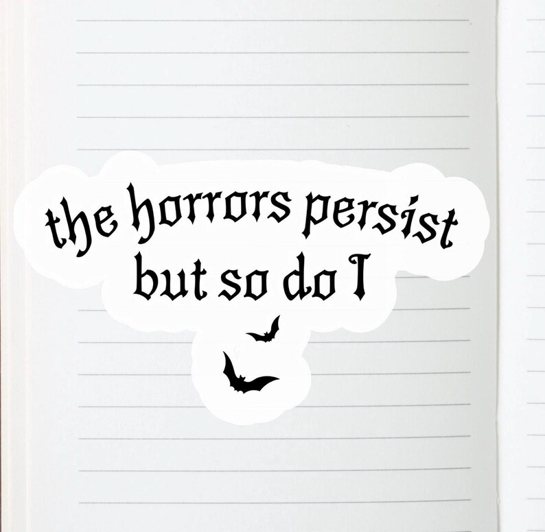 K&ouml;nnte beinhalten: Ein wei&szlig;er Aufkleber mit dem Text "the horrors persist but so do I" in gotischer Schrift. Zwei schwarze Fledermaus-Silhouetten befinden sich unter dem Text. Der Aufkleber befindet sich auf einer linierten Notizbuchseite.