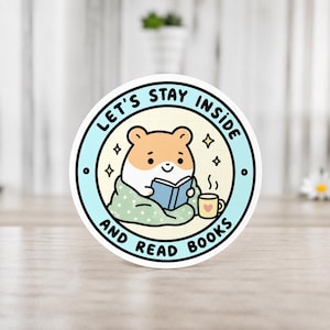 Könnte beinhalten: Runder Aufkleber mit einem Cartoon-Hamster, der unter einer Decke ein Buch liest, mit einer Tasse Kaffee. Der Aufkleber hat den Text "LET'S STAY INSIDE AND READ BOOKS" in einem hellblauen Kreis. Niedliches Design.