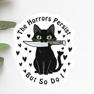 Könnte beinhalten: Ein schwarzer Katzenaufkleber mit grünen Augen, der ein Messer hält. Der Text "The Horrors Persist, But So Do I" ist um die Katze herum geschrieben, mit schwarzen Herzakzenten.