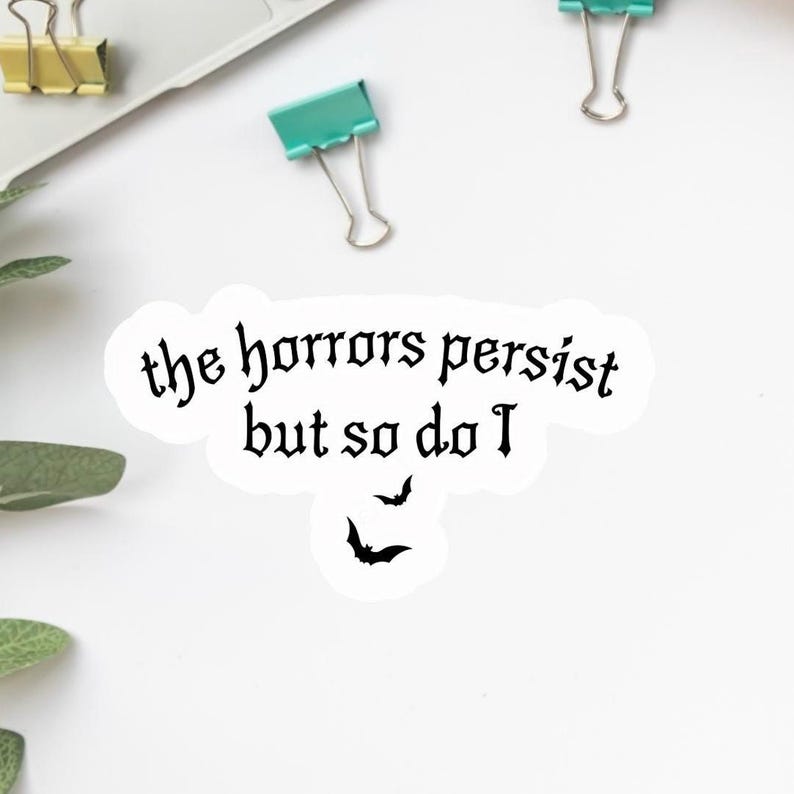 K&ouml;nnte beinhalten: Ein wei&szlig;er Aufkleber mit dem Text "the horrors persist but so do I" in gotischer Schrift. Darunter befinden sich drei schwarze Fledermaus-Silhouetten. Der Aufkleber befindet sich auf einer wei&szlig;en Oberfl&auml;che mit B&uuml;romaterial im Hintergrund.